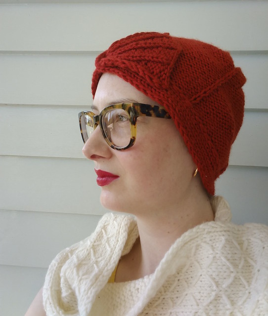 A woman wears a red cloche and white scarf.