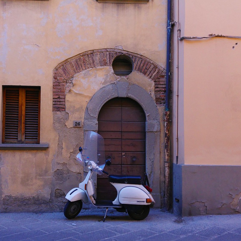 A motorbike parked against a yellow wall and rounded wooden door