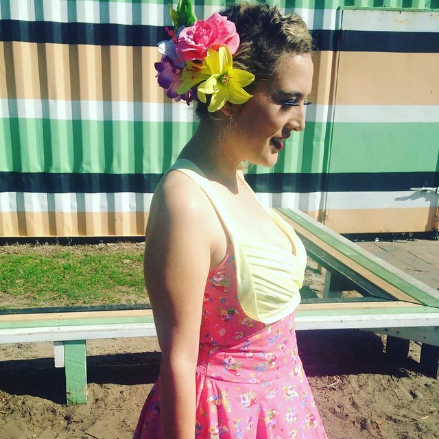 A woman wears a 50s-inspired shelf bust dress with matching floral headpiece.