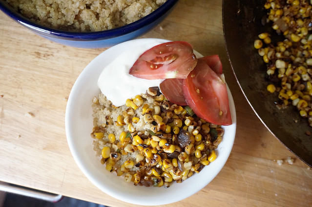 A charred corn quinoa bowl, with serving bowl of quinoa and wok full of corn still in frame, all shot at a slightly cockeyed angle