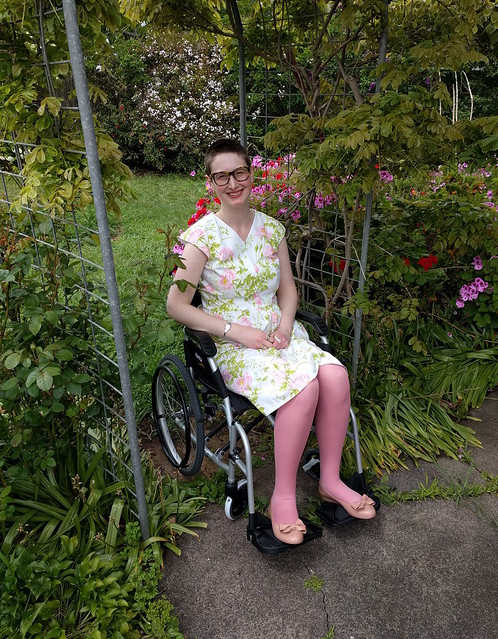 A woman poses in a wheelchair, wearing a 50s style frock in a floral print